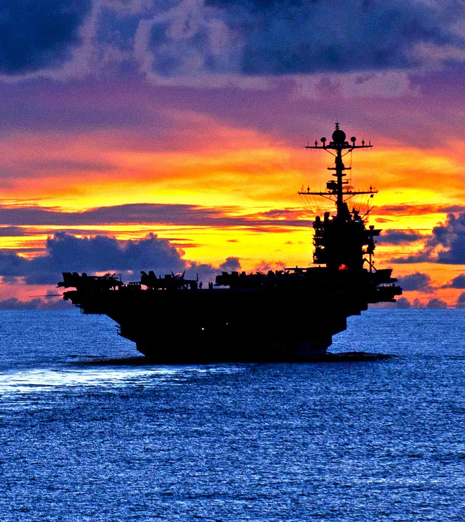 Silhouette of an aircraft carrier at sea against an orange sunset